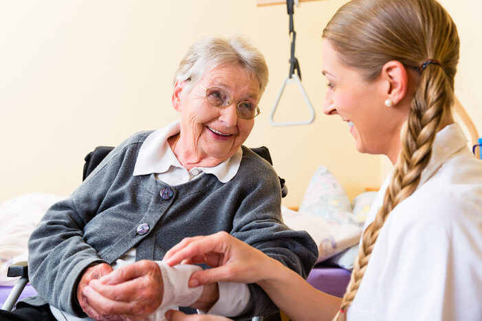 Nurse taking care of senior woman’s bandaged wound in senior rehabilitation